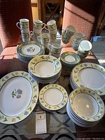 Photo of entire dinnerware set showing stacks of various plates, cups, and bowls with floral patterned rim.