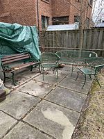 Two green metal mesh chairs, oval metal table and wooden slat bench arranged on patio pavers