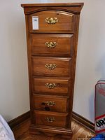 Front view of tall wooden highboy dresser with six drawers, brass handles, and carved base detail.