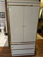 Front view of closed ivory armoire showing 2 doors and 2 large drawers with metallic handles and trim