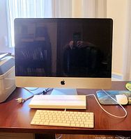 Front view of Apple iMac on desk with Magic Keyboard packaging, wireless keyboard in front, wired Apple mouse to side