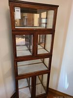 Photo of four stacked wooden and glass display cabinets with closed doors showing front and side glass panels.