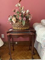Two wooden nesting tables with beveled glass inset tops side by side with woven basket with faux flowers on top.