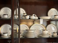 Full china cabinet display showing matching plates, cups, and serving pieces in Rochelle pattern.