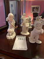 Three Snowbabies figurines displayed together showing a hockey player, skier, and snow shoe baby, with original auction lot card.