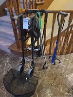 Photo showing black walker with seat and mesh basket, three canes including the 3-point and standard quad canes, and blue long-handled shoe horn attached.