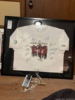 Framed white shirt with signatures and mounted light on top.