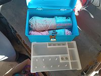 Blue plastic sewing box with white plastic organizer tray on top, containing yarn skeins in light pink and peach colors with labels showing 'Craft Yarn'.