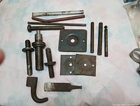 Various metal bolts, plates, and smaller components laid on cloth background, showing condition and type of parts.