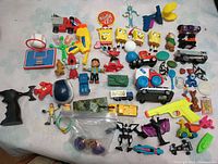 Photo showing various small plastic toys including action figures, toy vehicles, small sports toys, and character figures such as SpongeBob and Bugs Bunny