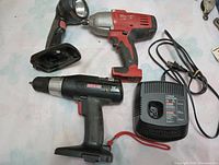 Photo showing Milwaukee red and black impact wrench, Craftsman cordless drill and battery charger, and flashlight without battery