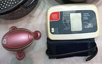 Pink handheld rolling massager with three rounded nodes, a digital blood pressure monitor, and cuff lying on a surface.