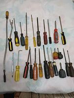 Photo showing 18 assorted screwdrivers with various handle designs and shaft lengths laid out on fabric background.