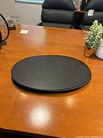 Stack of ten oval-shaped black leather placemats on a wood table.