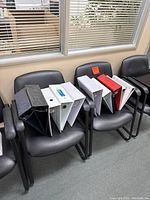 Eleven assorted ring binders placed on office chairs, showing different colors and sizes.