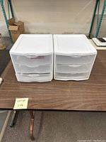 Front view of two identical white plastic storage cubbies with three drawers each placed side by side on a table.