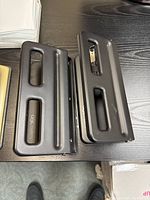 Two black metal three-hole punches placed side by side on a black desk showing top surface and handles