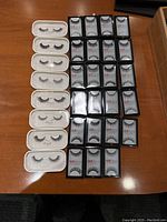 32 pairs of assorted faux eyelashes arranged on table, showing Esqido in white cases and Red Cherry in black boxes