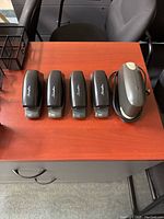Five electric staplers on a wooden desk, four black Swingline models and one larger gray model.