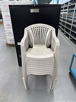 Front view of stack of eight light grey plastic chairs showing slatted back and armrests