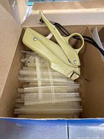 Beige vintage clothes tagger gun in box with plastic needles attached