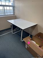 White drafting table in room, showing flat tabletop and metal legs.