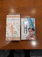 Photo showing two boxed Danielle facial cleansing tools: the Radiant system in peach and Glow system in white and blue, front and side views visible.