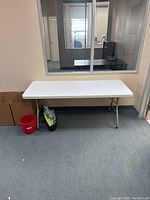 Front view of white rectangular folding table against a wall with window reflection.