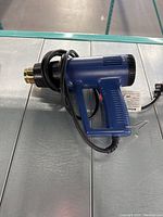 Blue electric heat tool with black and brass nozzle, adjustable heat settings, power cord wrapped around handle.
