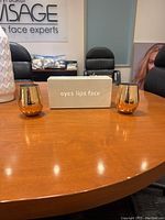 Photo showing two small brass-colored cups and a white rectangular holder with 'eyes lips face' text on a wooden table