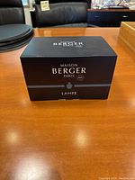 Front view of the black Maison Berger Paris Lampe box on a wooden table surface.