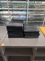 Black bubble mailer envelopes stacked in piles on a table in a warehouse setting.