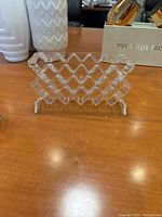 Front view of clear acrylic lipstick holder with a zigzag grid design and small feet, placed on a wooden surface.