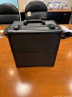 Full view of closed black makeup/tool case on a wood surface, showing latch closures and handle.
