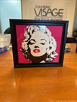 Front view of the Marilyn Monroe pop art framed picture on a wooden surface, showing the vibrant hot pink background and black and white artwork.