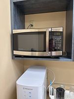 Danby stainless steel microwave with digital keypad and glass turntable inside shelf with outlet behind.
