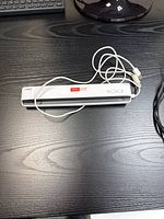 Front view of white Neat portable scanner with attached white USB cable on black wooden desk surface.