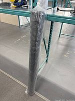 Full view of the roll of black plastic fencing mesh wrapped in clear plastic standing vertically against a metal shelving frame.