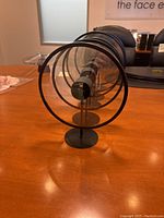 Five round metal picture frames with transparent centers arranged in a line on a wooden surface, shown from the front and side angles.