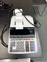 Front angled view of Sharp printing calculator showing keypad, display, and paper roll with printed receipt.