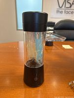 Front view of the small black and clear cylindrical drink mixer with power button on the base.