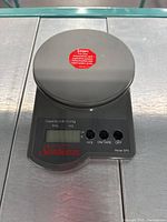 Front view of the Sunbeam digital scale showing the round platform, control buttons, and LCD display.