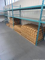 Stack of wooden slatted pallets in neat piles under blue metal shelving, showing quantity and condition