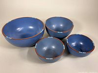 Four nested blue ceramic mixing bowls with brown rim and blue square accents, from largest to smaller sizes