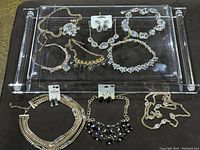 Full lot on clear display tray showing various gold toned necklaces and earrings with crystal decorations.