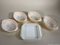 Four peach Lustreware casserole dishes with two clear glass lids, and one 8x8 square white glass baking dish.