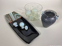 Set of all glass pieces showing the rectangular platter with swirled colors and orange dots, the raised glass bowl with dancing women, the black and white speckled blown glass vase with blue handles, and frosted glass eggs.