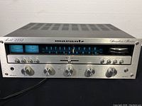 Angled front view of silver faceplate showing tuning display, meters lit blue and all control knobs