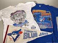Two XL Toronto Blue Jays T-shirts, white 1992 World Champions design and blue 1993 Spring Training, displayed with a white felt pennant flag and two buttons