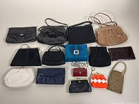 Full assortment of 14 vintage ladies clutches, handbags, coin purses in various materials and colors laid out for display